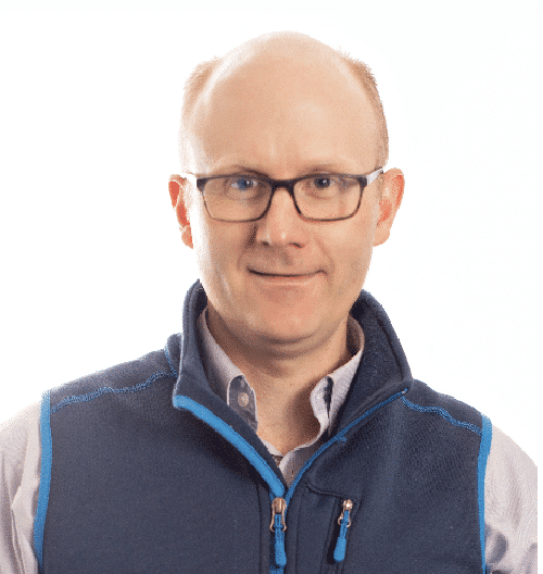 Man with glasses wearing a blue zippered vest over a light shirt, facing the camera with a slight smile.
